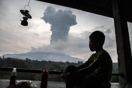 Sumatra und Java, Indonesien: Der Vulkan Sinabung auf Sumatra spuckt Asche und Feuer. Dass der Junge dabei so gelassen am Fenster sitzt, liegt wohl daran, dass solche Naturkatastrophen auf Sumatra und Java Standard sind. Von Erdbeben bis zu Vulkanausbrüchen und Tsunamis erleben die Menschen hier tödliche Gefahren.  