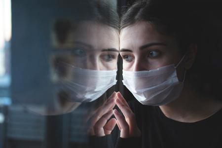 Frau mit Maske spiegelt sich am Fenster