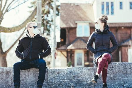 Mann und Frau sitzen mit Abstand und Maske in der Sonne