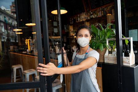 Gastronomin öffnet Tür mit Maske