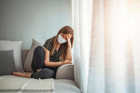 traurige Frau mit Maske auf Couch