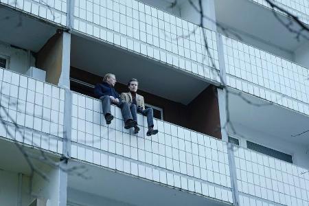 Klaus (Ben Becker) und Henry (Anton von Lucke, r.) sitzen auf der Balkonbrüstung; Henry will sich um Saras Beerdigung kümmern