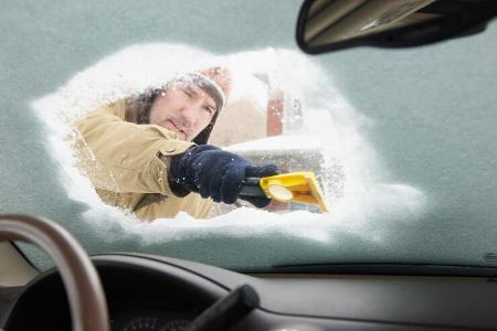 Caucasian man scraping snow off car windshield