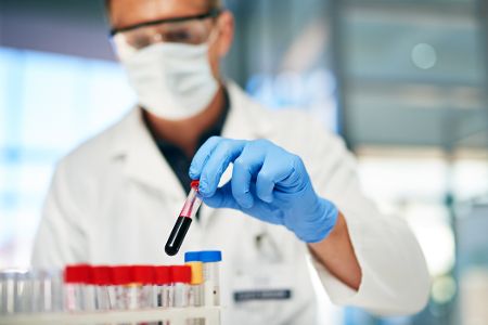 Forscher steckt Röhrchen mit Blut in einen Ständer im Labor