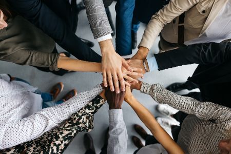 Menschen stehen im Kreis und halten die Hände in der Mitte zusammen, von oben gesehen