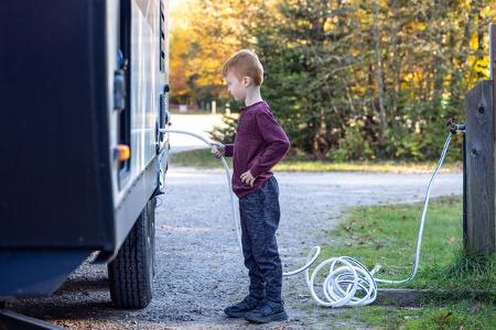 Little Boy Connecting Water Hose to Camper Trailer on Campground in Autumn, Quebec, Canada Little Boy Connecting Water Hose to Camper Trailer on Campground in Autumn, Quebec, Canada