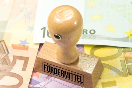 Stempel mit Aufdruck Fördermittel steht auf Geldscheinen