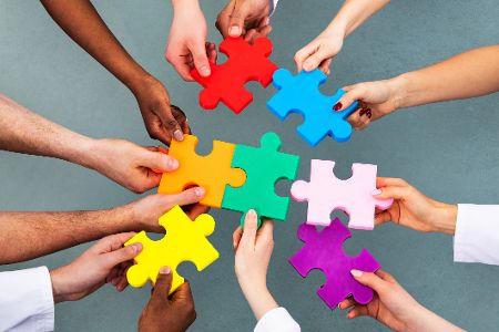 Verschiedene Hände halten Puzzleteile, die ein Gesamtbild ergeben