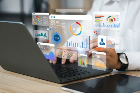 Laptop mit einer arbeitenden Person, über dem verschiedene Grafiken schweben