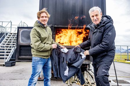 Salzburg Research-Forscher Severin Bernhart und Texport-Geschäftsführer Otmar Schneider mit einem Prototyp einer intelligenten Feuerwehrjacke vor der Brandsimulationsanlage