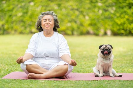 Ältere Frau sitzt mit Hund auf Yogamatte