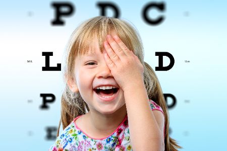 Kind hält sich Auge zu, im Hintergrund sind die Buchstaben eines Sehtests zu sehen. Kind hält sich Auge zu, im Hintergrund sind die Buchstaben eines Sehtests zu sehen.
