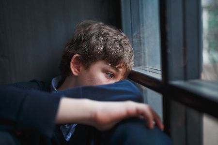 Jugendlicher sitzt drinnen am Fenster