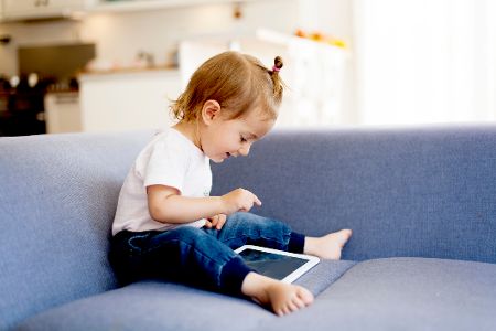Kleines Kind sitzt mit Tablet auf dem Sofa