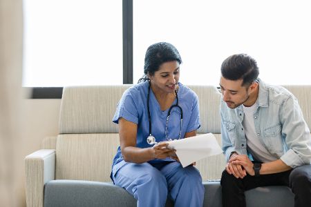Ärztin erklärt Patienten anhand eines Klemmbretts etwas