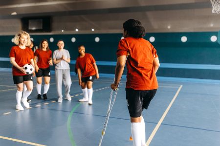 Verletzte Handballspielerin humpelt auf Krücken auf das Spielfeld zu ihren Kolleginnen