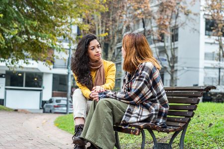 Zwei junge Frauen sitzen auf der Bank und unterhalten sich Zwei junge Frauen sitzen auf der Bank und unterhalten sich