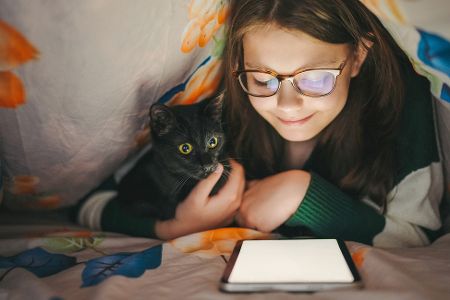 Kind liegt mit Katze zusammen unter einer Decke und liest an einem Kindle Kind liegt mit Katze zusammen unter einer Decke und liest an einem Kindle