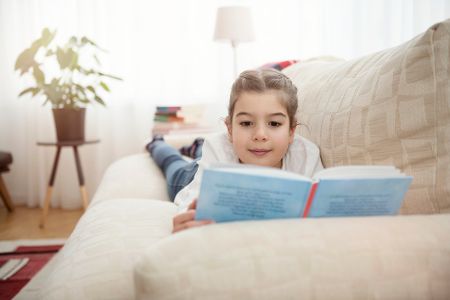 Mädchen liegt auf dem Sofa und liest in einem Buch