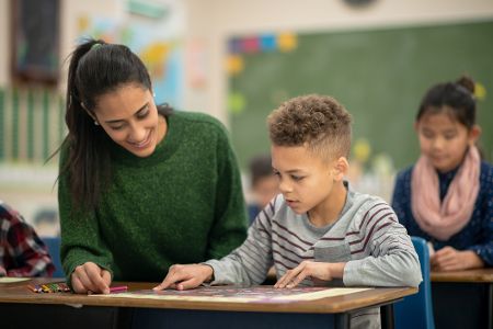 Lehrerin sitzt neben einem Jungen im Unterricht und erklärt ihm etwas