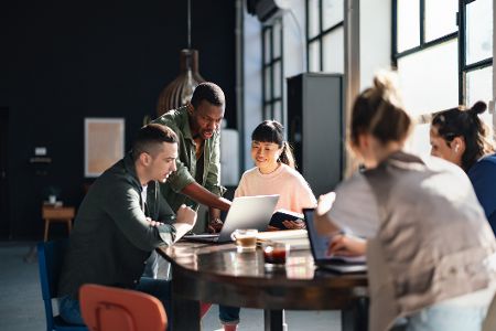 Junge Erwachsene sitzen um einen Tisch bei der Arbeit