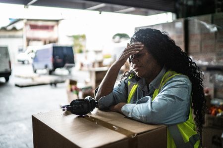 Arbeiterin steht im Lager und hält sich den schmerzenden Kopf