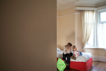 Frau sitzt mit ihrem kleinen Kind auf einem Bett, neben sich eine Tüte mit Kleidung