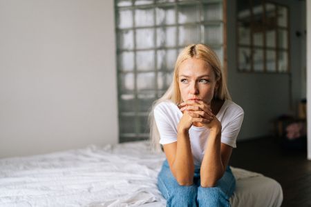Frau sitzt alleine und traurig auf einem Bett