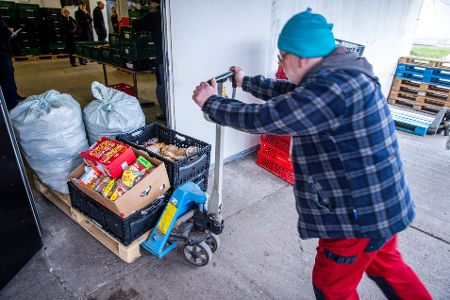 Mensch schiebt einen Wagen voll mit Lebensmittelspenden in ein Haus
