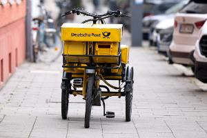 Ein Fahrrad eines Briefträgers steht auf einem Gehweg - auch dieser Briefträger möchte vermutlich gern deutlich besser bezahlt werden.