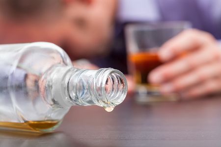 Mann liegt mit Kopf auf Tisch, vor ihm eine leere Flasche Alkohol
