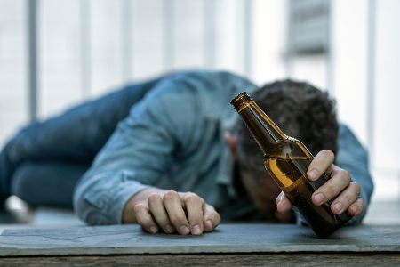 Mann liegt auf dem Fußboden, in der Hand eine Bierflasche