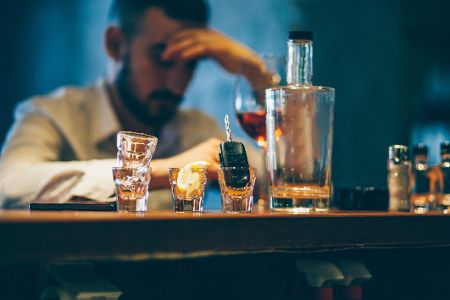 Mann sitzt vor mehreren Schnapsgläsern und einer Flasche Alkohol