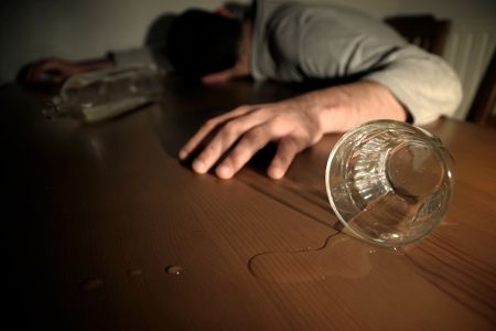 Mensch liegt auf dem Tisch, neben ihm ein Glas und eine Flasche Alkohol
