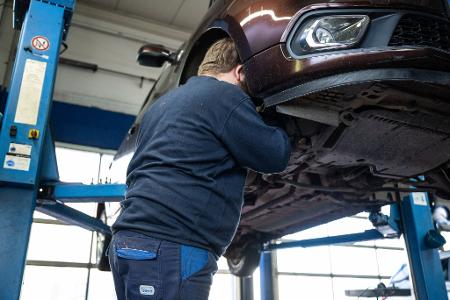 Ein Mechaniker schaut in einer Kfz-Werkstatt in den Radkasten eines Autos.