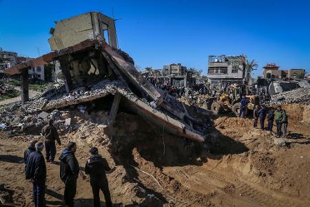 Palästinenser beobachten, wie Mitarbeiter des Zivilschutzes Leichen aus den Trümmern eines durch einen israelischen Luftangriff zerstörten Hauses bergen.