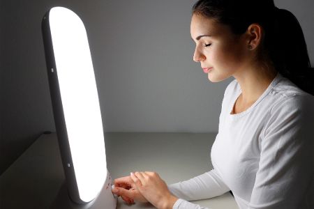 Frau sitzt vor einer Tageslichtlampe