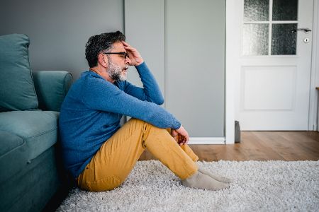 Depressiver Mann sitzt vor einem Bett auf dem Fußboden