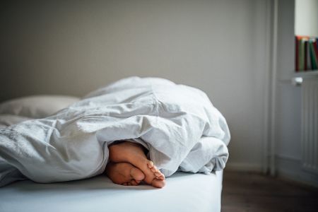Zwei Füße schauen unter einer Bettdecke hervor