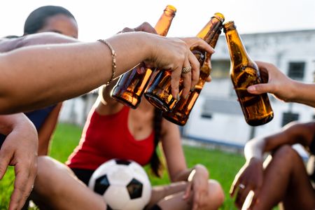 Spieler und Spielerinnen sitzen mit einem Fußball in der Mitte zusammen und trinken Bier