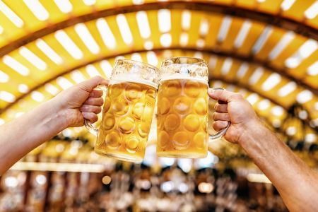 Zwei Hände mit Bierkrügen stoßen in einem Festzelt miteinander an
