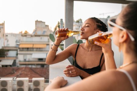 Zwei Frauen sitzen in einer Bar über den Dächern einer Stadt und trinken Bier