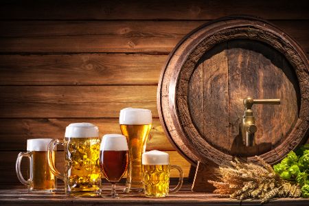 Verschiedene Biersorten in Gläsern vor einem Bierfass