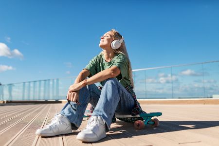 Frau sitzt draußen in der Sonne, hört Musik über Kopfhörer und ist glücklich Frau sitzt draußen in der Sonne, hört Musik über Kopfhörer und ist glücklich