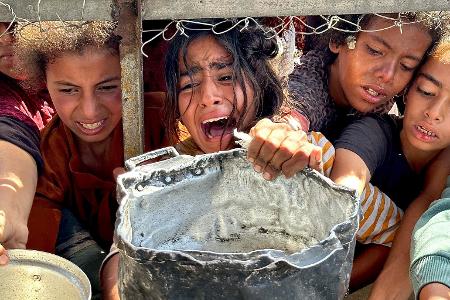 Palästinensische Kinder versuchen im Gebiet Al-Mawasi im Gazastreifen, mit ihren Töpfen Nahrungsmittel zu bekommen, die von Wohltätigkeitsorganisationen verteilt werden.