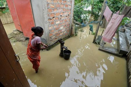 Eine Frau versucht in der überfluteten Umgebung ihres Hauses, Wasser zu sammeln. 