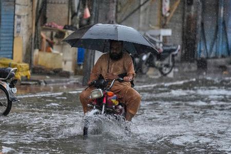Mit aufgespanntem Regenschirm fährt ein Motorradfahrer waghalsig durch die Monsunfluten.