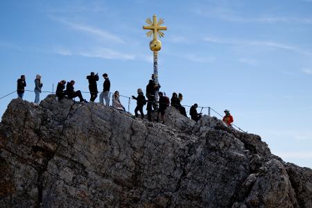 Ausflügler genießen das schöne Wetter am Gipfelkreuz auf der Zugspitze.