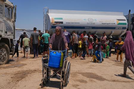 Eine palästinensische Frau schiebt einen Rollstuhl mit Plastikkanistern mit Wasser im Gazastreifen.