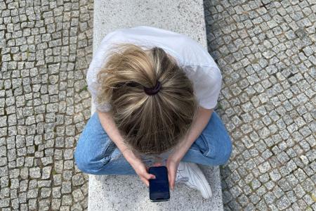 Typische Haltung in heutiger Zeit: mit gesenktem Kopf auf das Handy schauen. Typische Haltung in heutiger Zeit: mit gesenktem Kopf auf das Handy schauen.